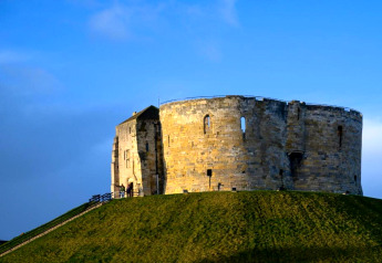 Ronde stenen burchttoren op een groene heuvel onder een blauwe lucht, opvallend historisch gebouw.