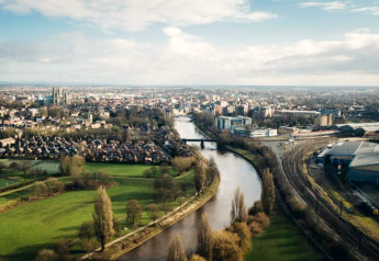 Luchtfoto van een rivier die door een stad stroomt, met groene parken, spoorwegen en woonwijken zichtbaar.