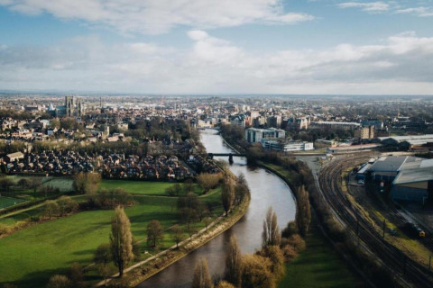 Aerial view of a river winding through a city, with parks, rail tracks, and residential neighborhoods visible.