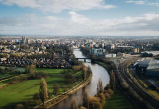 Aerial view of a river winding through a city, with parks, rail tracks, and residential neighborhoods visible.