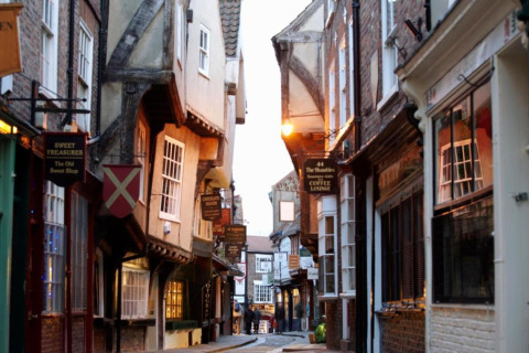 Narrow, picturesque street with old timber-framed houses and hanging shop signs in the evening light.