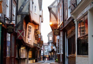 Narrow, picturesque street with old timber-framed houses and hanging shop signs in the evening light.
