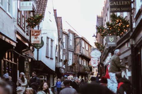 Bustling historic alleyway with people shopping, festive decorations, and quaint, timber-framed shops.