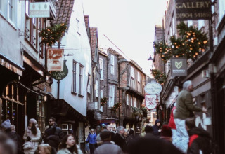 Bustling historic alleyway with people shopping, festive decorations, and quaint, timber-framed shops.