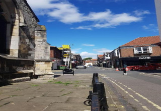 A street scene with historic stone buildings, shops, a ladder, and clear blue sky with white clouds.