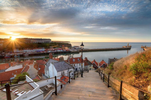 Sunset over a picturesque harbor town with red roofs, quay, piers, and a stairway leading down to the sea.