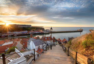 Sunset over a picturesque harbor town with red roofs, quay, piers, and a stairway leading down to the sea.