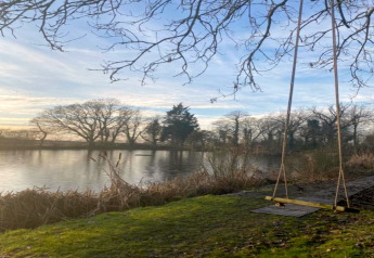 Blik op de vijver en schommel bij de ‘Worm Dale’-pod in het Verenigd Koninkrijk, tussen kale bomen.