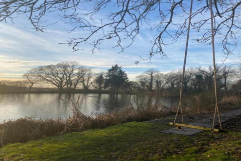 Vue de l’étang et d’une balançoire au pod « Worm Dale » au Royaume-Uni, avec des arbres nus et de l’eau calme.