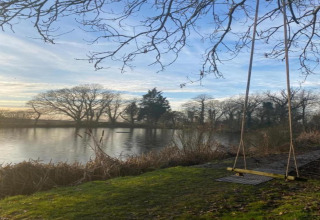 Vue de l’étang et d’une balançoire au pod « Worm Dale » au Royaume-Uni, avec des arbres nus et de l’eau calme.