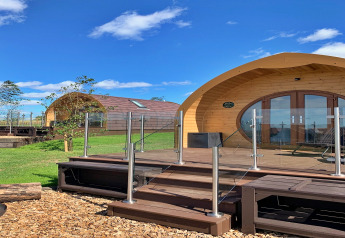 Gebogen houten pods en glazen balustrade bij Worm Dale in het VK, omringd door groen gras en blauwe lucht.