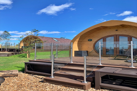 Pods en bois courbés avec balustrade en verre à Worm Dale au Royaume-Uni sous un ciel bleu et clair.
