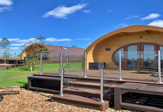 Pods en bois courbés avec balustrade en verre à Worm Dale au Royaume-Uni sous un ciel bleu et clair.