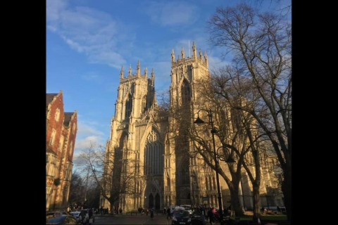 Photo taken from a pod, showing a majestic Gothic cathedral under a bright blue sky with tall trees.