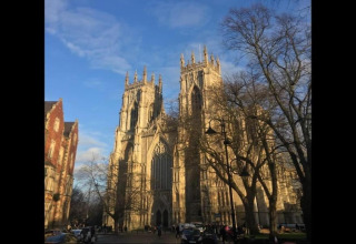 Photo taken from a pod, showing a majestic Gothic cathedral under a bright blue sky with tall trees.