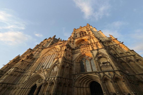 Majestic Gothic cathedral captured from below at dusk, golden sunlight highlighting its intricate facade details.