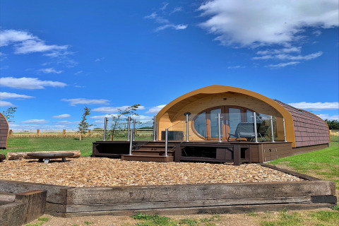 Glamping-pod ved navn Mingle Dale i Storbritannien, med trægulv, terrasse og klar blå himmel.