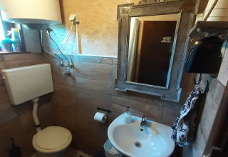 Compact bathroom in a chalet featuring a toilet, sink, mirror, water heater and tiled walls.