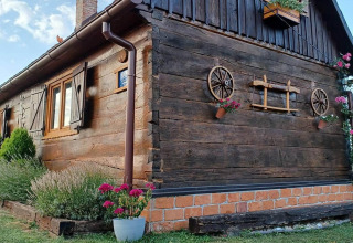 Sfeervol houten chalet in Kroatië met bloemen en oude wagenwielen aan de buitenmuur als decoratie.