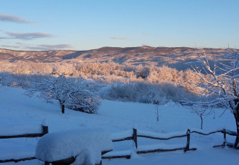 Paesaggio innevato dal chalet Stara Hiža Vlašić in Croazia con alberi illuminati dal sole e colline.