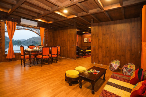 Elegante interno di houseboat con pannelli in legno, tende arancioni e vista lago da grandi finestre panoramiche.