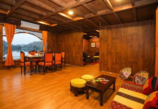 Elegante interno di houseboat con pannelli in legno, tende arancioni e vista lago da grandi finestre panoramiche.