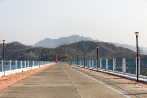 Breiter Gehweg mit Laternen, blauem Zaun und Bergblick, fotografiert von Ekta Houseboat Statue Of Unity.