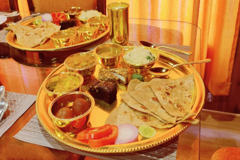 Indisches Thali auf goldenem Tablett mit verschiedenen Currys, Chapati, Reis und Dessert auf Hausboot.