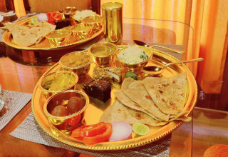 Indisches Thali auf goldenem Tablett mit verschiedenen Currys, Chapati, Reis und Dessert auf Hausboot.