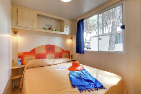 Lichte slaapkamer in het Luna Pineta mobilhome in Italië, met tweepersoonsbed en groot raam.