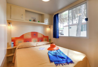 Lichte slaapkamer in het Luna Pineta mobilhome in Italië, met tweepersoonsbed en groot raam.
