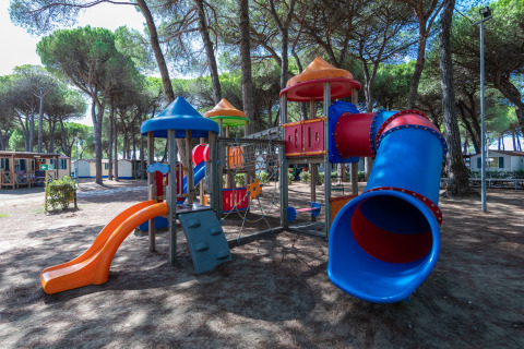 Kleurrijke speeltuin met glijbanen bij mobilhome Luna Pineta in Italië, onder hoge bomen geplaatst.