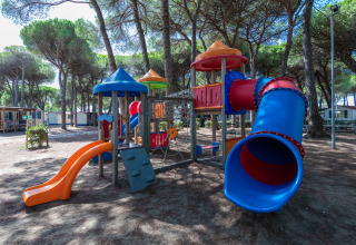 Kleurrijke speeltuin met glijbanen bij mobilhome Luna Pineta in Italië, onder hoge bomen geplaatst.