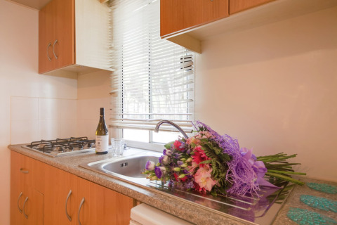 Keuken in de Luna Pineta stacaravan in Italië met bloemenboeket, fles wijn en glas bij het raam.