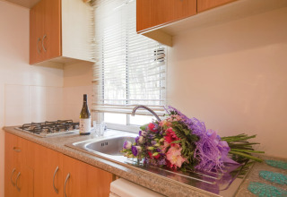 Keuken in de Luna Pineta stacaravan in Italië met bloemenboeket, fles wijn en glas bij het raam.