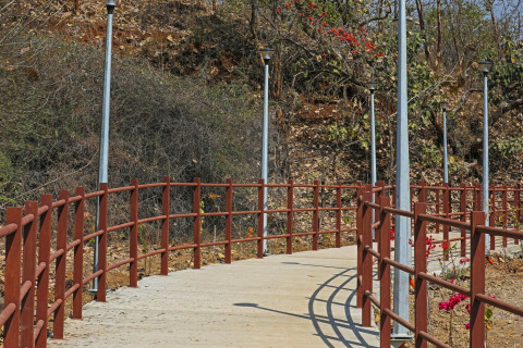 Fußweg mit roten Geländern und Straßenlaternen bei Ekta Houseboat Statue Of Unity, umgeben von Trockenvegetation.