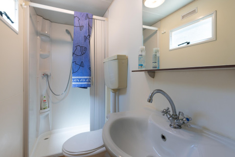 Badkamer in de stacaravan 'Luna Pineta' in Italië met douche, wastafel, toilet en spiegel.