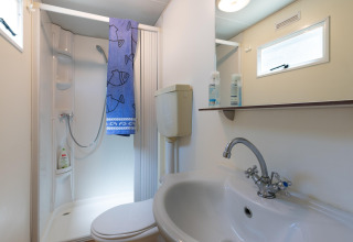 Badkamer in de stacaravan 'Luna Pineta' in Italië met douche, wastafel, toilet en spiegel.