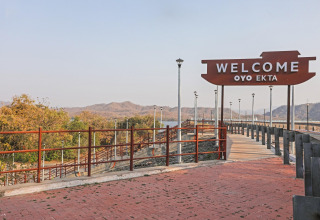 Cartello di benvenuto alla Ekta Houseboat Statue of Unity Kevadia, con paesaggio collinare sullo sfondo.