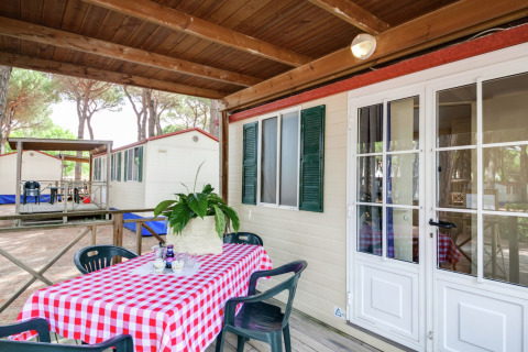 Stacaravan met overdekt terras, tafel met rood geruite tafelkleed en plant, Luna Pineta, Italië.
