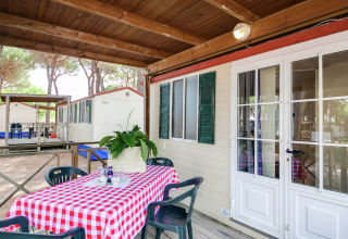 Stacaravan met overdekt terras, tafel met rood geruite tafelkleed en plant, Luna Pineta, Italië.