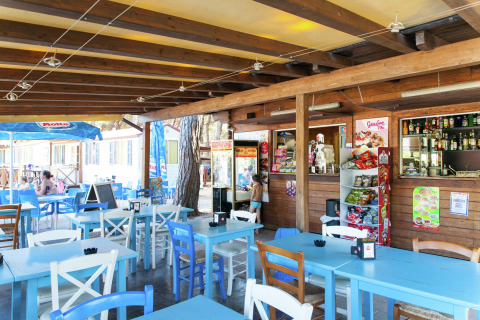 Buitencafé bij mobil home Luna Pineta in Italië met blauwe en witte tafels en stoelen.