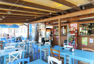 Buitencafé bij mobil home Luna Pineta in Italië met blauwe en witte tafels en stoelen.