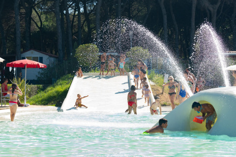 Kinderen spelen in het waterpark bij mobilhome Luna Pineta in Italië, met glijbanen en waterstralen.