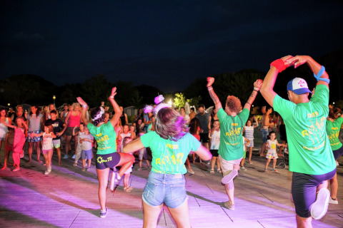 Mensen dansen samen 's avonds voor de Luna Pineta stacaravan in Italië, gekleed in groene shirts.