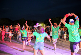 Mensen dansen samen 's avonds voor de Luna Pineta stacaravan in Italië, gekleed in groene shirts.
