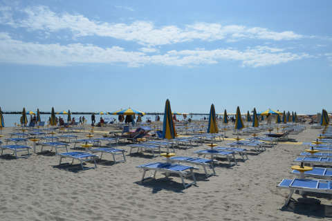 Strand met blauwe en gele parasols en ligstoelen bij mobilhome Luna Pineta in Italië.