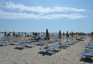 Strand met blauwe en gele parasols en ligstoelen bij mobilhome Luna Pineta in Italië.