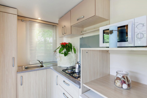 Moderne Küchenzeile im Mobilheim Cottage Cesenatico in Italien mit Herd, Spüle, Mikrowelle und Dekoration.