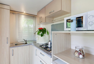 Moderne Küchenzeile im Mobilheim Cottage Cesenatico in Italien mit Herd, Spüle, Mikrowelle und Dekoration.